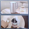 A Xiaomi electric kettle and a glass pitcher are shown on a wooden table in the top image. The bottom image shows a hand holding the electric kettle with its lid open, next to a glass of water and a book. Náhľad obrázku produktu