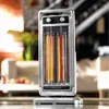 A silver and black halogen heater with glowing orange heating elements is placed on a table in a living room setting. Náhled obrázku produktu