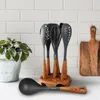 A set of kitchen utensils on a countertop with a plant and a cutting board in the background. Anteprima dell’immagine prodotto