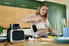 A woman is in a kitchen, pouring liquid from a blender jug into a pan. Produktbild-Vorschau