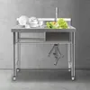 A stainless steel sink with dishes and vegetables in it, set against a concrete wall. Náhled obrázku produktu