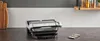 A modern kitchen counter with a grill, cutting board, and jars of spices on a shelf. Voir les images du produit