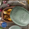A Römertopf casserole dish with a cooked chicken inside, placed on a wooden surface with onions and spices. Produktbild-Vorschau