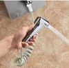 A hand holding a shower head with water spraying out, attached to a coiled hose, with a tiled wall in the background. Náhľad obrázku produktu