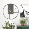 A modern minimalist wall clock is displayed on a white wall, next to a piece of abstract art and a potted plant. Produktbild-Vorschau