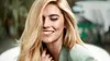 A woman with blonde hair smiling and looking down, with her hand near her neck. Náhled obrázku produktu