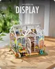 A miniature greenhouse model with plants and gardening tools displayed on a wooden surface. Podgląd zdjęcia produktu