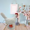 A white chicken-shaped lamp with an orange foot sits on a wooden surface next to a jewelry stand with pearls and a vase of flowers. Podgląd zdjęcia produktu