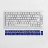 A white mechanical keyboard and a set of blue keycaps with white icons are displayed on a textured white surface. Produktbild-Vorschau