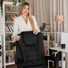 A woman in a white suit stands behind a black office chair in a well-lit room with bookshelves and a desk. Produktbild-Vorschau