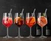 Four cocktail glasses with drinks and straws, set against a dark background with bottles in the background. Náhľad obrázku produktu