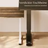 Close-up of the base of two desk legs, one black and one white, with a wooden tabletop visible at the top. Text overlays describe features. Produktbild-Vorschau