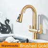 A brushed gold kitchen faucet with a pull-down sprayer is shown in a sink area, next to a decorative black swan sculpture and a dish drying rack. Podgląd zdjęcia produktu
