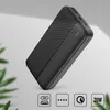 A black power bank is shown diagonally on a light gray and white background with green leaves in the foreground. Produktbild-Vorschau