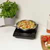A frying pan filled with vegetables is placed on an induction cooktop, next to a potted basil plant and some tomatoes and garlic on a cutting board. Voir les images du produit