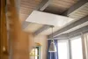 A modern room with wooden ceilings and beams, featuring a white ceiling infrared heater and a pendant light. Produktbild-Vorschau