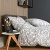 A bedroom scene with a bed dressed in paisley patterned bedding, a bedside table with a vase of dried flowers and a laptop. Produktbild-Vorschau