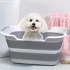 A small white dog is sitting in a gray and white collapsible pet bathtub. Produktbild-Vorschau