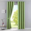 A pair of green curtains are shown tied back, with a window view of a green lawn and trees behind them. A small side table with decorative items is to the left. Produktbild-Vorschau