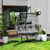 A hanging egg chair with cushions is placed on a green lawn in front of a modern house with wooden siding. Produktbild-Vorschau