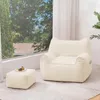 A beige beanbag chair and ottoman are placed in a well-lit room with a large window overlooking trees and a house. Náhled obrázku produktu