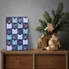 A Christmas advent calendar is displayed on a wooden dresser next to a vase with a Christmas tree branch and decorations. Náhľad obrázku produktu