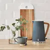A kitchen counter scene with a kettle, a mug with a tea bag, and a vase with greenery. Podgląd zdjęcia produktu