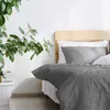 A bed with grey bedding and white pillows, next to a large potted plant. Produktbild-Vorschau