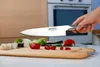 A hand holding a knife over a cutting board with sushi and vegetables. Anteprima dell’immagine prodotto