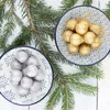 Two bowls of decorative food powder, one gold and one silver, are placed on a white wooden surface with pine branches. Anteprima dell’immagine prodotto