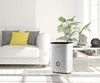 A white humidifier is placed on a light-colored floor next to a white sofa and a coffee table with plants and decorative items. Produktbild-Vorschau