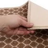 A hand is shown lifting the corner of a rug to reveal its backing. Podgląd zdjęcia produktu