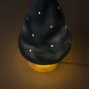 A close-up shot of a black mushroom-shaped lamp with small white dots, emitting a warm yellow light from its base. Produktbild-Vorschau