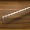 A brushed metal cabinet handle is placed on a wooden surface. Produktbild-Vorschau