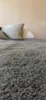 A close-up view of a textured gray blanket or throw, with a blurred light brown and white object in the background. Produktbild-Vorschau