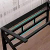 Close-up view of the black metal frame of a gaming desk, with a hint of wood flooring and sheer curtains in the background. Blue light accents are visible beneath the frame. Podgląd zdjęcia produktu