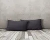Two dark gray rectangular pillows are placed on a light-colored wooden floor against a textured gray wall. Produktbild-Vorschau