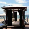 A cabana with black curtains on a beach with umbrellas and boats in the background. Náhled obrázku produktu