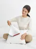 A woman is sitting on a bed and using a white handheld vacuum cleaner with a red base on a white pillow. Produktbild-Vorschau