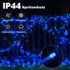 Blue string lights are draped over a wooden fence, with some decorative ornaments hanging from the fence. The image has text overlays indicating product features. Produktbild-Vorschau