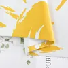 A close-up view of a folded yellow and white patterned fabric, likely a curtain, with a hint of greenery and text from a book or magazine in the background. Produktbild-Vorschau
