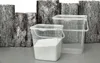 Two transparent plastic storage containers with handles are placed on a gray surface in front of a rustic wooden background. Produktbild-Vorschau