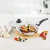 A frying pan with pancakes and berries on a wooden board, with a lid and utensils nearby. Produktbild-Vorschau