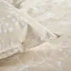 A close-up view of beige bedding with a white floral pattern. Produktbild-Vorschau