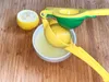 A manual citrus juicer with a lemon being squeezed into a white bowl. Produktbild-Vorschau