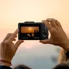 Hands holding a digital camera, capturing a sunset scene. Produktbild-Vorschau