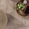 A close-up view of a rug with a woven pouf, a woven basket with a candle, greenery, and a book. Produktbild-Vorschau