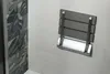 A wall-mounted folding shower seat is shown in a bathroom setting. Anteprima dell’immagine prodotto