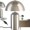 Three silver mushroom-shaped table lamps are shown against a white background. One lamp is in the foreground, and two are in the background. A small portion of a wooden cabinet is visible on the right side, with a small lamp on it. Náhled obrázku produktu