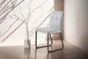 A light gray upholstered dining chair with black metal legs is placed next to a glass vase with branches on a reflective surface, with dramatic shadows cast on the wall. Náhled obrázku produktu